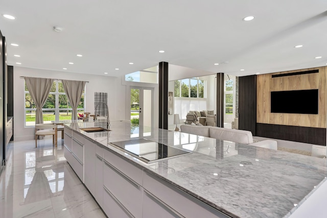 kitchen with white cabinetry, sink, light stone countertops, black electric cooktop, and a spacious island