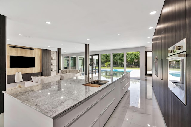 kitchen with sink, white cabinetry, a large island with sink, light stone counters, and stainless steel oven