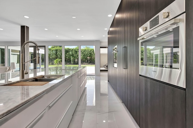 kitchen featuring sink, oven, white cabinets, dark brown cabinetry, and light stone countertops