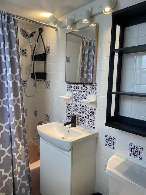 full bathroom featuring tile walls, decorative backsplash, vanity, toilet, and shower / bathtub combination with curtain