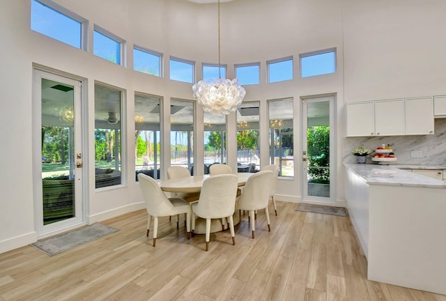 dining space featuring a notable chandelier, a towering ceiling, and light wood-type flooring