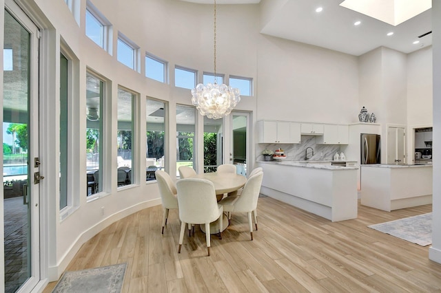 dining area with a towering ceiling, a skylight, sink, a notable chandelier, and light hardwood / wood-style flooring