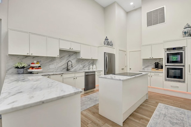 kitchen with sink, a center island, light hardwood / wood-style flooring, stainless steel appliances, and white cabinets