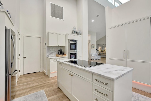 kitchen with a center island, high vaulted ceiling, stainless steel appliances, light hardwood / wood-style floors, and white cabinets