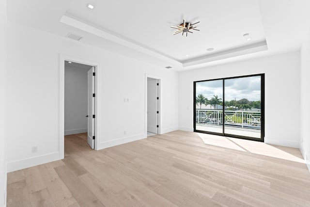 spare room with light wood-type flooring and a tray ceiling