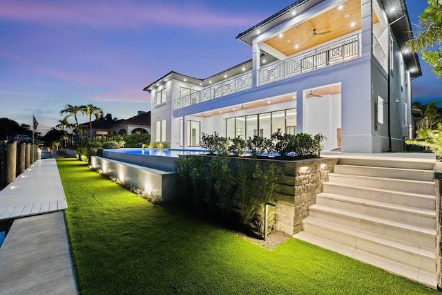 back house at dusk featuring a fenced in pool, a yard, and a balcony