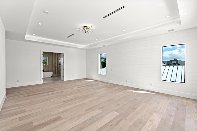 spare room with a raised ceiling and light hardwood / wood-style flooring