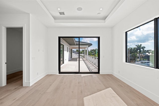 spare room with a tray ceiling and light wood-type flooring