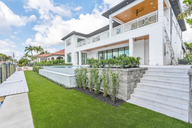 rear view of property with a lawn, a balcony, and ceiling fan