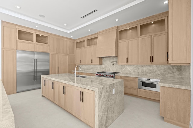 kitchen with sink, a kitchen island with sink, premium appliances, light stone countertops, and custom range hood