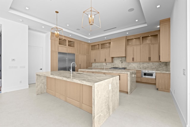 kitchen with a large island with sink, a raised ceiling, appliances with stainless steel finishes, and custom exhaust hood