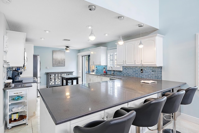 kitchen featuring pendant lighting, white cabinetry, sink, backsplash, and kitchen peninsula