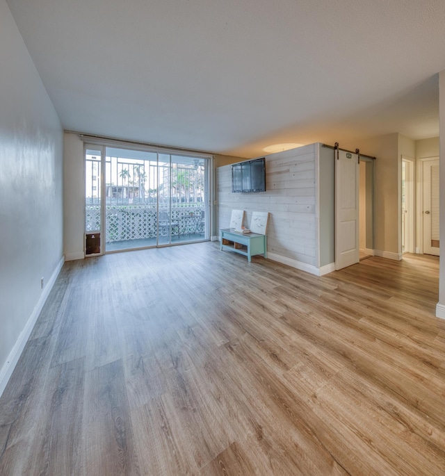 1 S Lakeside Dr Unit A2, Lake Worth Beach, FL 33460 - unfurnished living room with a barn door, light wood-style flooring, baseboards, and a wall of windows