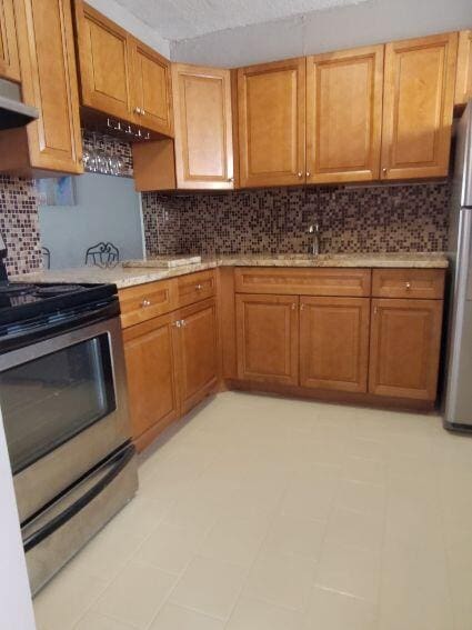 kitchen featuring backsplash, stainless steel appliances, light countertops, under cabinet range hood, and a sink