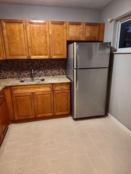 kitchen featuring freestanding refrigerator, brown cabinets, a sink, and decorative backsplash