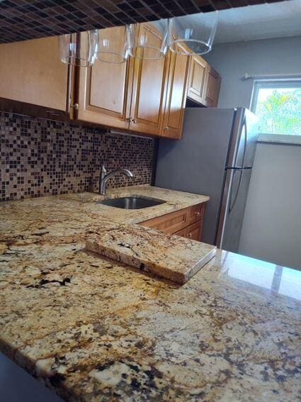 kitchen with tasteful backsplash, freestanding refrigerator, a sink, and light stone counters