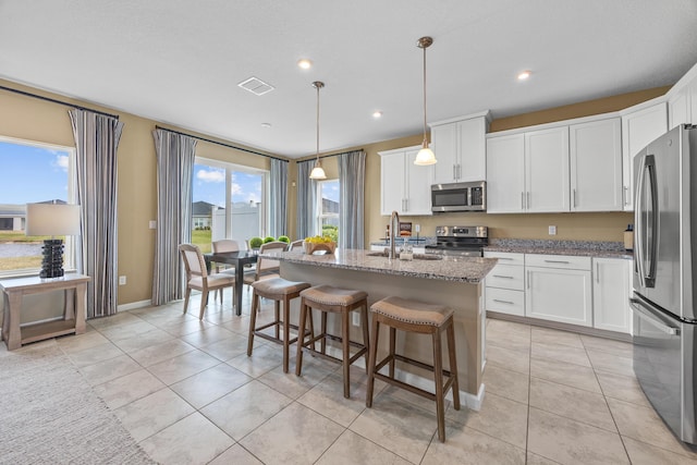 kitchen with hanging light fixtures, appliances with stainless steel finishes, a center island with sink, and white cabinetry