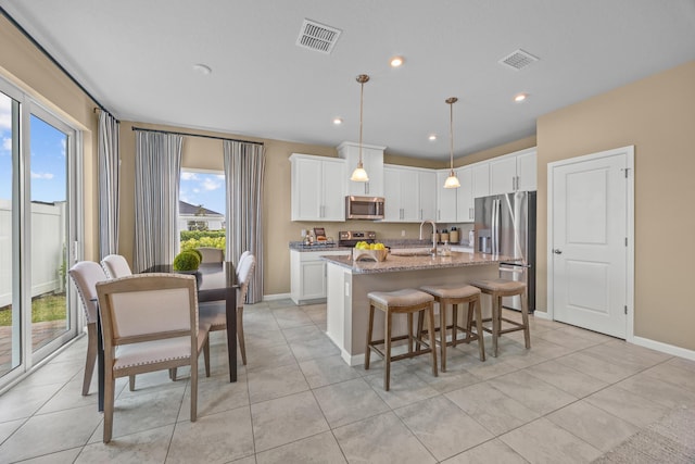 kitchen with stainless steel appliances, visible vents, white cabinetry, a center island with sink, and pendant lighting