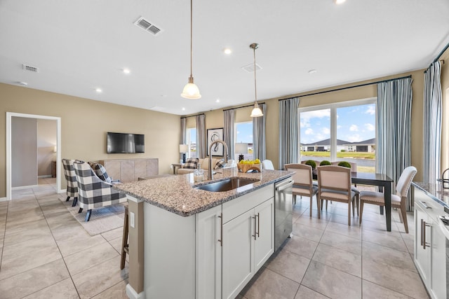 kitchen with a sink, visible vents, white cabinetry, light stone countertops, and a center island with sink