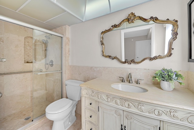 full bathroom featuring toilet, a wainscoted wall, vanity, tile walls, and a shower stall