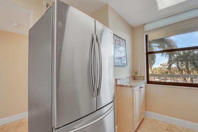 kitchen featuring light tile patterned floors, light stone countertops, baseboards, and freestanding refrigerator