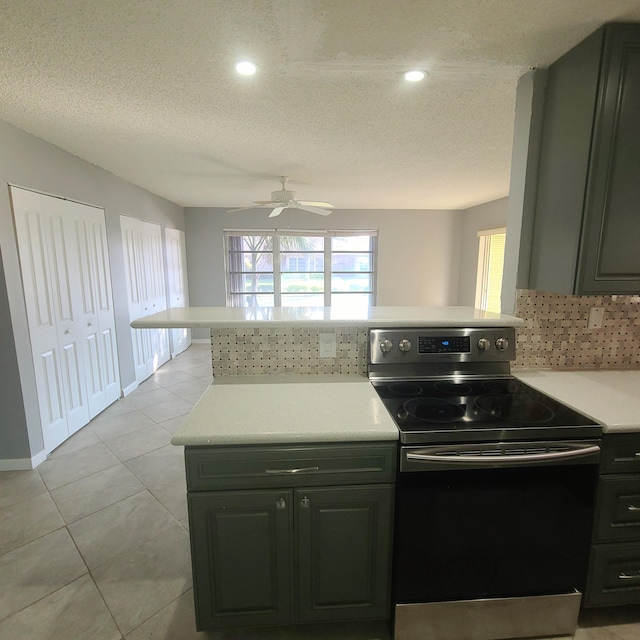 kitchen featuring light tile patterned flooring, stainless steel range with electric cooktop, ceiling fan, kitchen peninsula, and a textured ceiling