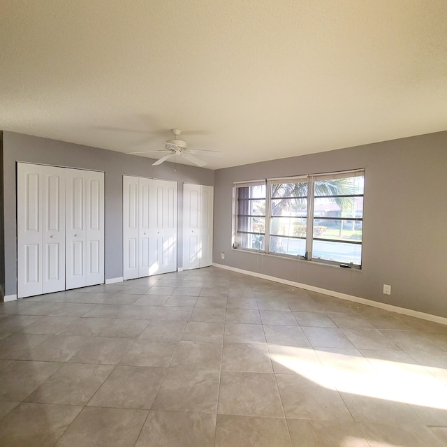 unfurnished bedroom featuring two closets, ceiling fan, and light tile patterned floors