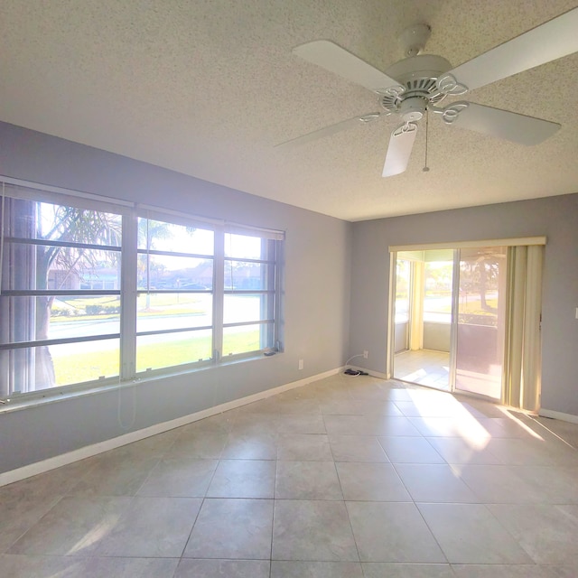 tiled spare room with ceiling fan, a wealth of natural light, and a textured ceiling