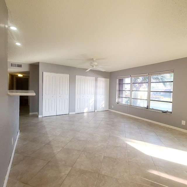 unfurnished bedroom with light tile patterned floors, two closets, and ceiling fan