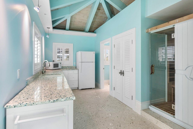 kitchen with lofted ceiling with beams, white cabinets, light stone countertops, white appliances, and baseboards