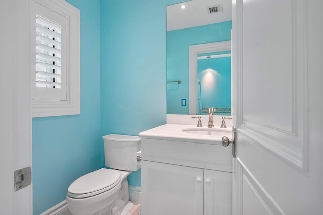 half bath with baseboards, visible vents, vanity, and toilet