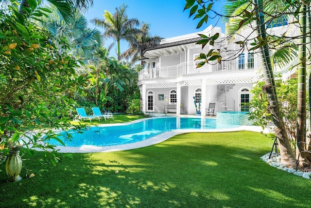 rear view of property featuring an outdoor pool, a lawn, and a balcony