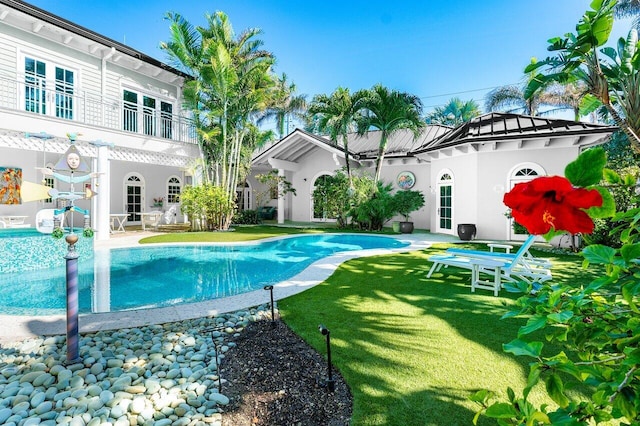 back of property with metal roof, a balcony, an outdoor pool, a standing seam roof, and stucco siding