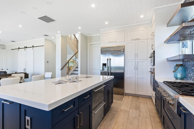 kitchen featuring a warming drawer, a kitchen island, a barn door, appliances with stainless steel finishes, and wall chimney exhaust hood