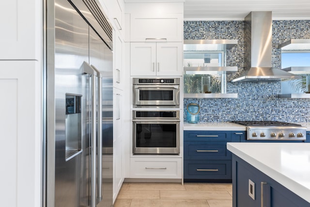 kitchen with stainless steel appliances, light countertops, white cabinets, wall chimney exhaust hood, and tasteful backsplash