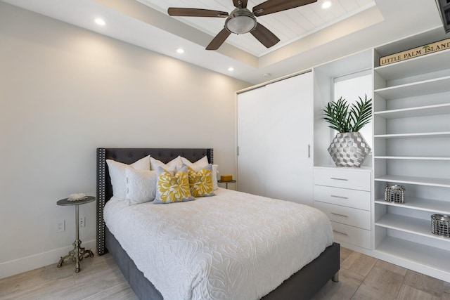 bedroom featuring a raised ceiling, recessed lighting, light wood-type flooring, and baseboards