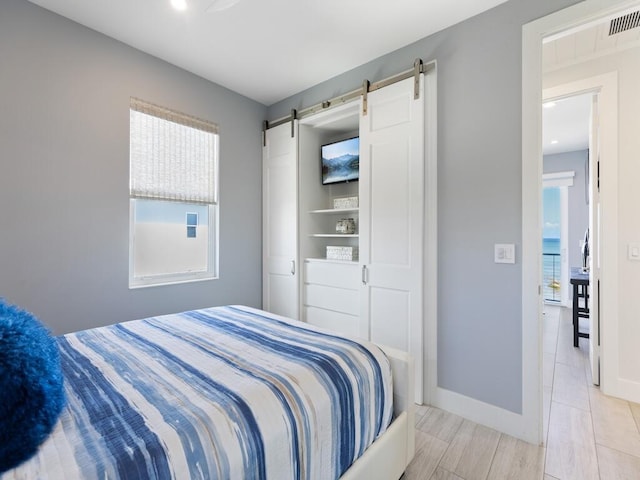 bedroom featuring a barn door, multiple windows, baseboards, and visible vents