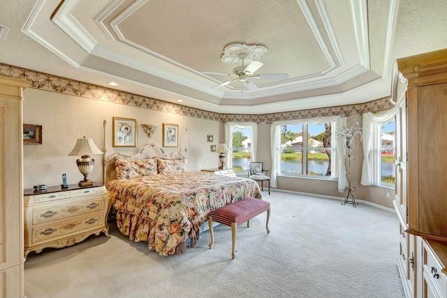 bedroom with ornamental molding, ceiling fan, a tray ceiling, a water view, and light carpet