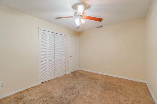 unfurnished bedroom featuring light carpet, ceiling fan, a closet, and a textured ceiling