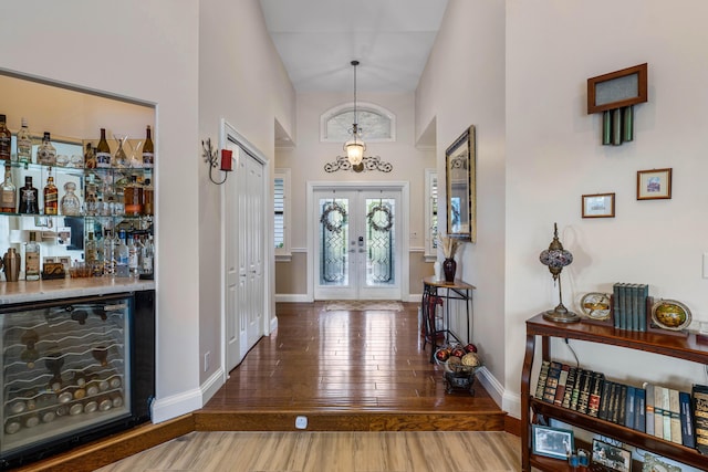 entrance foyer with hardwood / wood-style flooring, bar, a towering ceiling, french doors, and beverage cooler