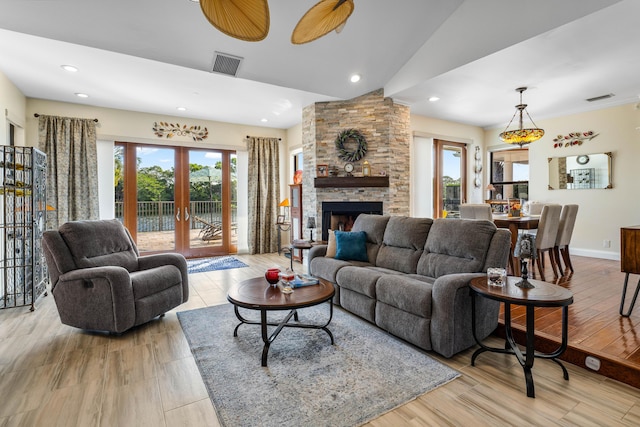 living room featuring vaulted ceiling, a fireplace, light wood-type flooring, and french doors