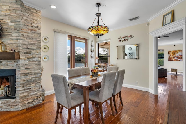 dining area featuring a fireplace, crown molding, dark wood-type flooring, and a healthy amount of sunlight