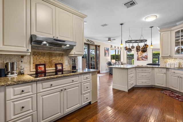 kitchen with dark hardwood / wood-style floors, black electric stovetop, decorative light fixtures, kitchen peninsula, and dark stone counters