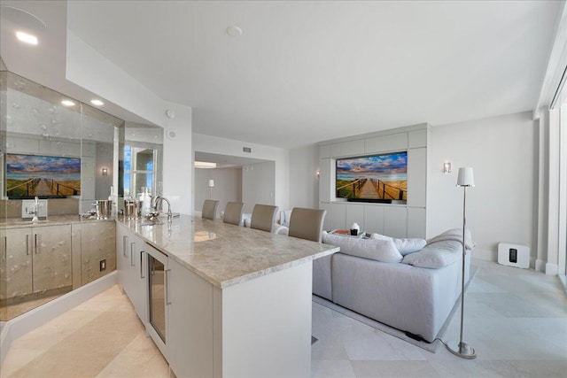 kitchen featuring a kitchen bar, sink, light stone counters, kitchen peninsula, and beverage cooler