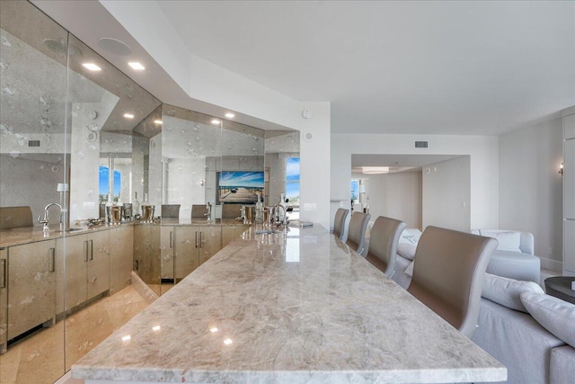 kitchen with light stone countertops, sink, light brown cabinets, and a breakfast bar