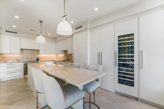 kitchen with pendant lighting, backsplash, light stone countertops, white cabinets, and a kitchen island