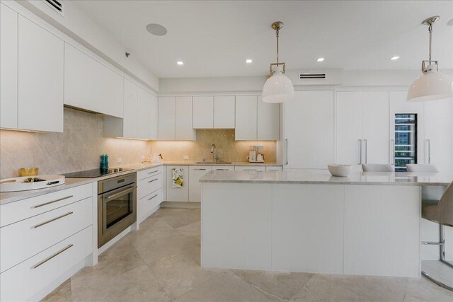 kitchen with sink, wine cooler, light stone counters, a kitchen bar, and kitchen peninsula