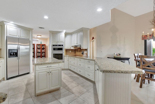 kitchen featuring light tile patterned floors, appliances with stainless steel finishes, white cabinets, a kitchen island, and decorative backsplash