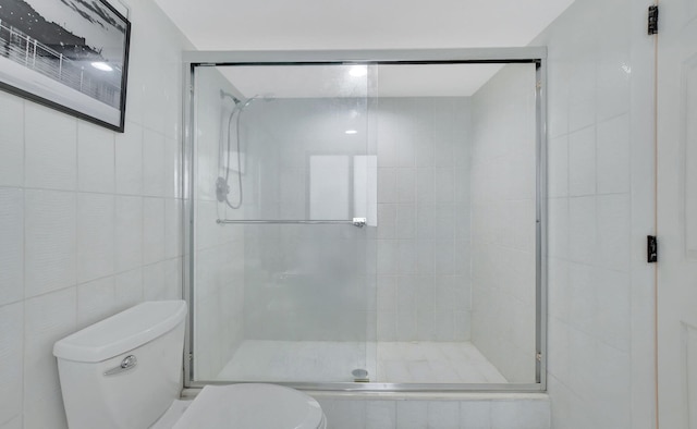 bathroom featuring toilet, a shower with door, and tile walls