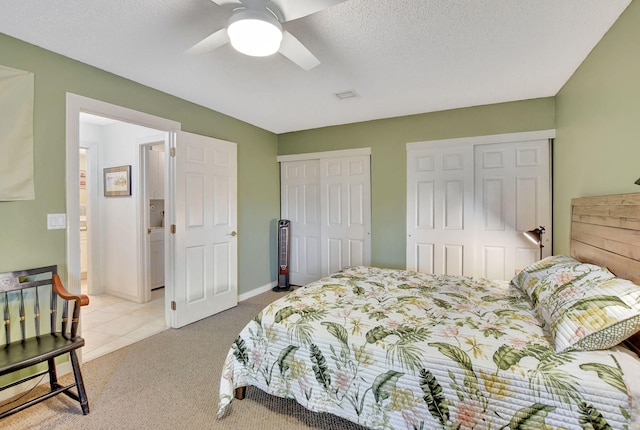 bedroom with light carpet, ceiling fan, a textured ceiling, and multiple closets